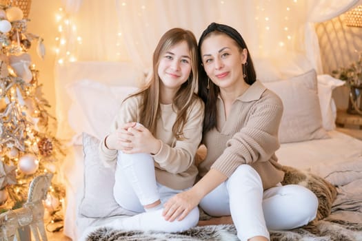 Happy mom and daughter cuddle on bed in decorated bedroom on Christmas Eve in anticipation of the party