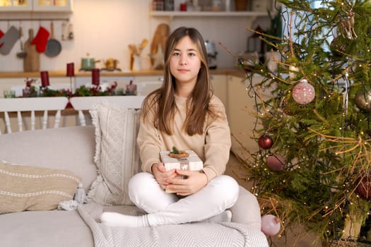 A cute girl sits on the couch with a Christmas present from her family