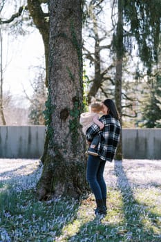 Mom with a little girl in her arms stands in a clearing among flowering crocuses near a tree. High quality photo