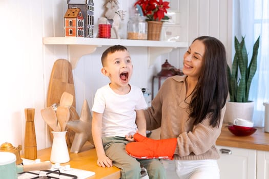 Fun mom and son playing in kitchen, happy spending time on Christmas Eve and New Year's Eve