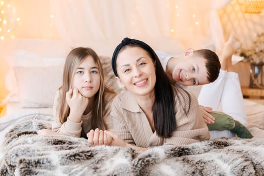 Happy family mom and two kids lying on bed waiting for Christmas and laughing