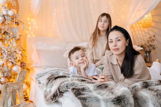 Mom and kids lying on bed in decorated bedroom and laughing concept winter holidays with the family