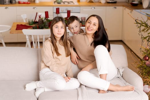 Family spends time together during Christmas holidays in decorated house. Mother and her two children hug each other as they prepare for holiday. Selective focus