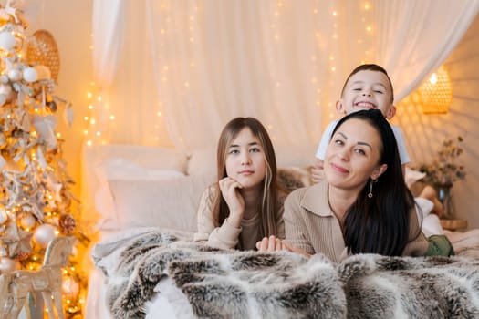 Happy family mom and two kids lying on bed waiting for Christmas and laughing