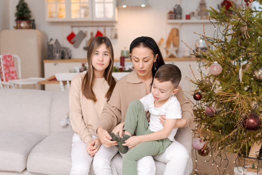 Family spends time together during Christmas holidays in decorated house. Mother and her two children hug each other as they prepare for holiday. Selective focus