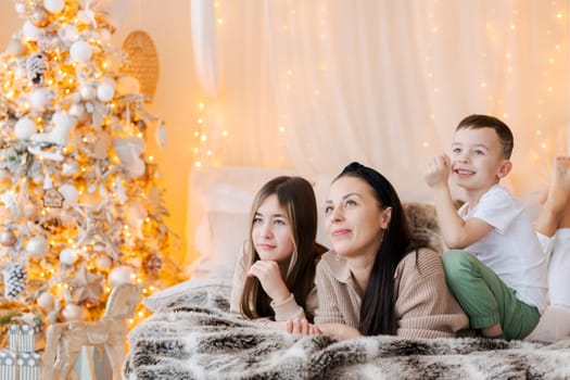 Happy family mom and two kids lying on bed waiting for Christmas and laughing