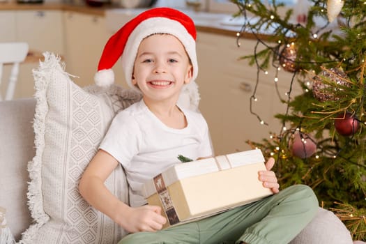 Cute little boy in Santa hat sits on couch with Christmas present from his family