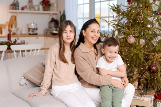 Family spends time together during Christmas holidays in decorated house. Mother and her two children hug each other as they prepare for holiday. Selective focus