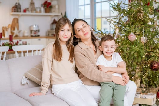 Family spends time together during Christmas holidays in decorated house. Mother and her two children hug each other as they prepare for holiday. Selective focus