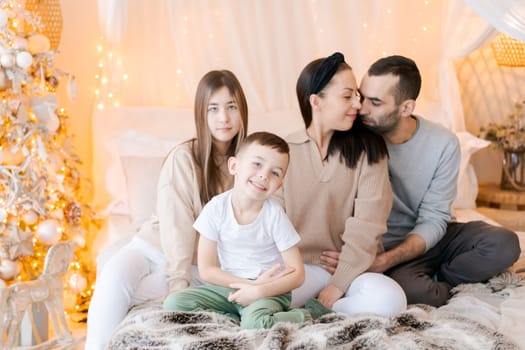 Happy family children and parents on bed in decorated bedroom at Christmas waiting for the holiday and laughing