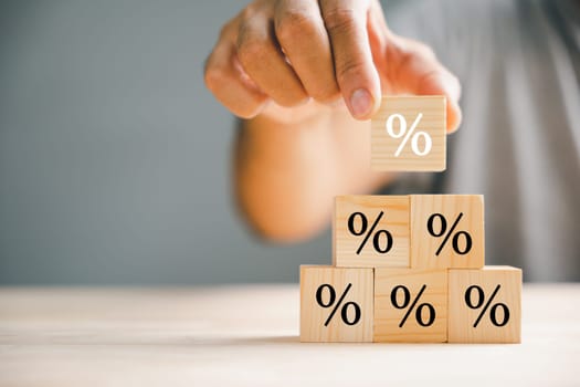 Illustrating the concept of interest rate and financial ranking. Businessman's hand placing a wooden cube block with a percentage symbol icon, representing the dynamic nature of rates.