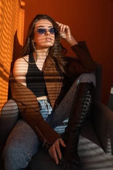 Woman wearing sunglasses posing in an armchair on an orange background at sunset