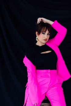 Woman in bright suit posing on black background in studio