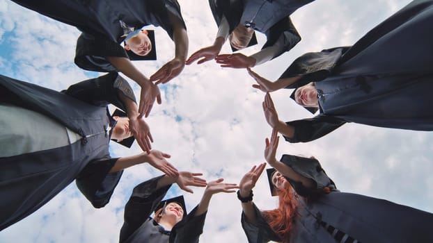 College graduates make a circle of their hands