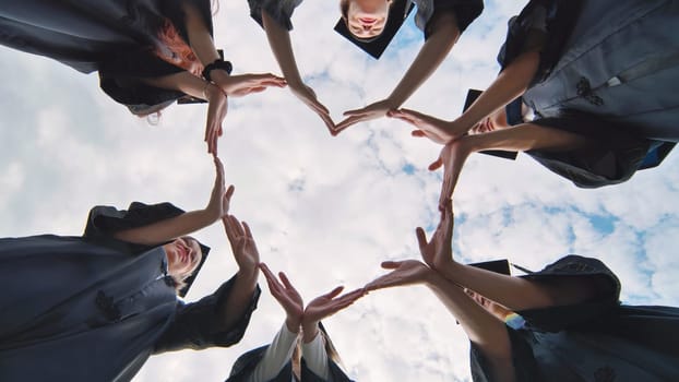 Students graduating from the college make a heart out of their hands