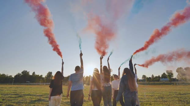 A group of friends spraying multi-colored smoke at sunset