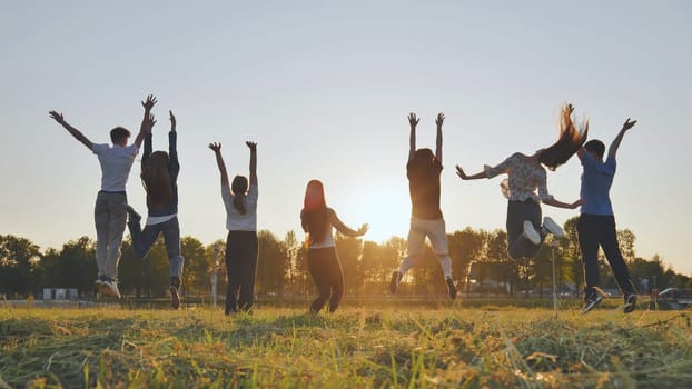 Group of five happy friends jumps at sunset time on background mountains