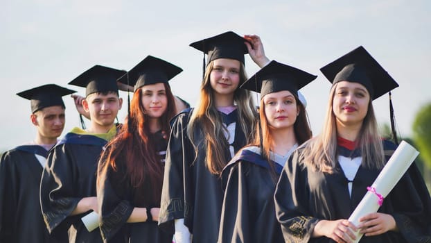 Cheerful graduates pose with raised diplomas on a sunny day