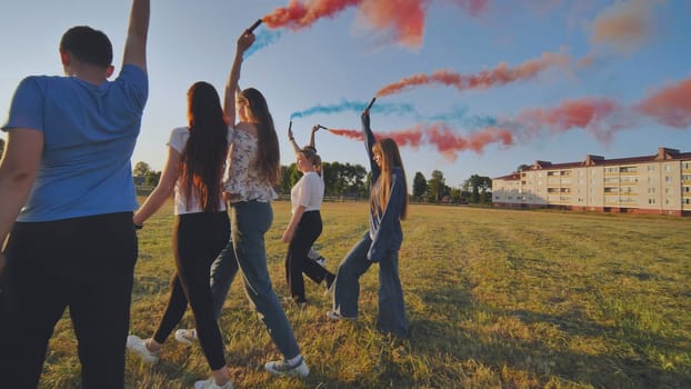 A group of friends spraying multi-colored smoke at sunset