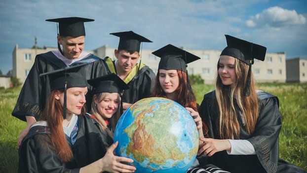 Graduates in black robes examine a geographical globe sitting on the grass