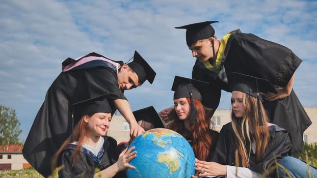 Graduates in black robes examine a geographical globe sitting on the grass