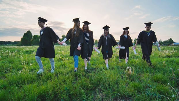 Six graduates in robes walk against the backdrop of the sunset