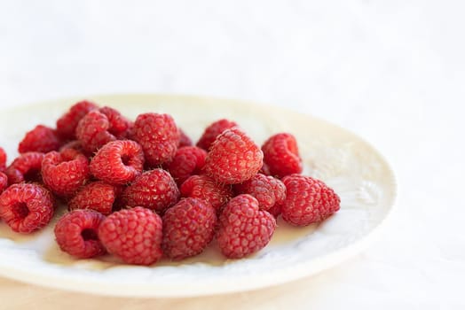 Fresh, ripe raspberries on a white plate, set against a white tablecloth. Perfect for a healthy snack or dessert