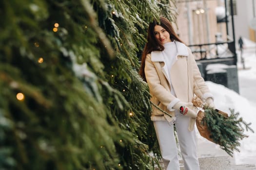 A girl with long hair in winter on the street with a bouquet of fresh fir branches.