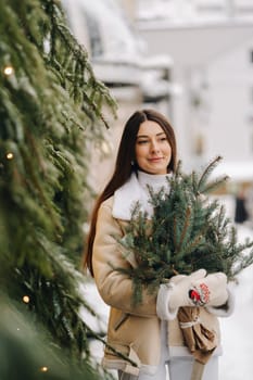 A girl with long hair in winter on the street with a bouquet of fresh fir branches.