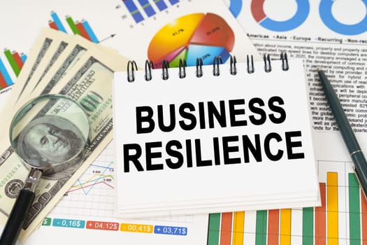 Business concept. On the table are business charts, dollars and a notepad with the inscription - business resilience