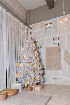 Christmas tree with silver and blue decorations and lights. Cozy Christmas tree and gift boxes on a white wall background