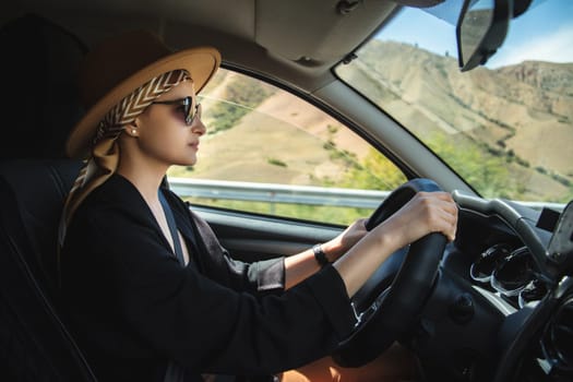 Stylish young woman in a hat is driving a car.