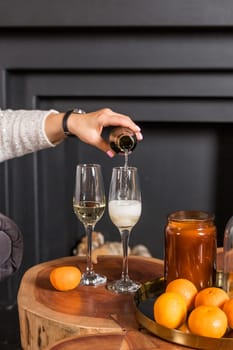 Two glasses of champagne and tangerines on a table against blurred christmas background with christmas lights. New year celebration party