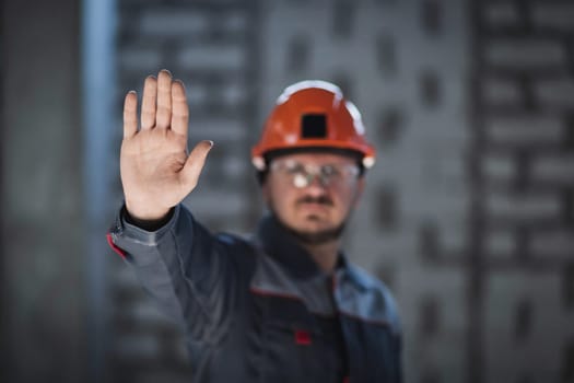 A worker in overalls and a hard hat shows an open palm demonstrating a refusal to work, a crisis in the workplace, a workers' strike.