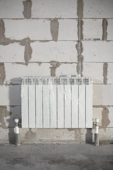 Installed aluminum heating radiators in rough finish during building construction, piping in the floor screed, copy space, vertical.