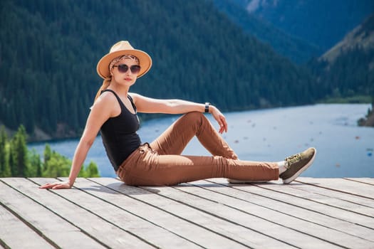 A young woman in safari style went out to nature outside the city, taking a weekend tour to the Kolsai mountain lake in the Tien Shan mountains, copy space