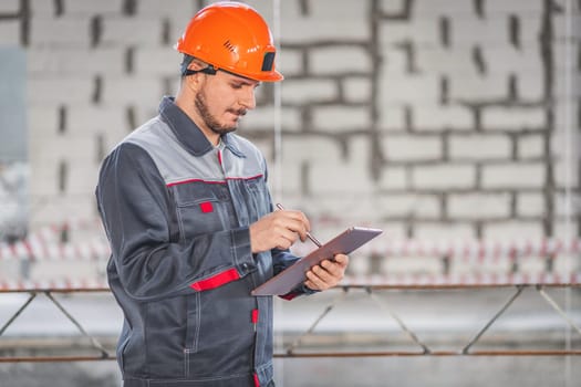 A builder looks at a project on a digital tablet and checks the plans of a house being built on a construction site, copy space.