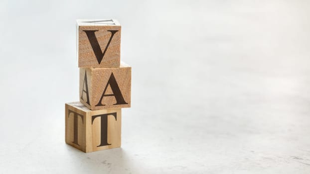 Pile with three wooden cubes - letters VAT meaning Value Added Tax on them, space for more text / images at right side.