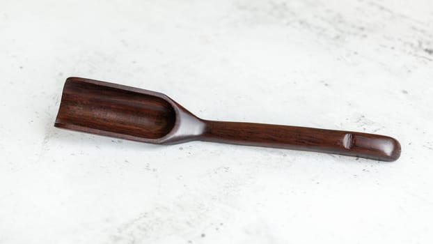 Narrow spice / tea spoon made of dark wood, on white working board.