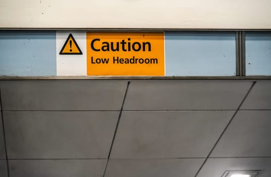 Orange " Caution low headroom " sign on roof above elevators