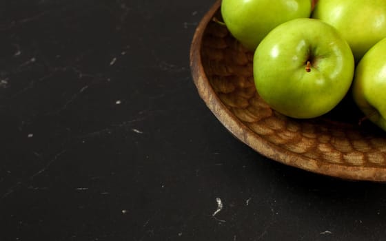 Green apples on wooden carved bowl, only part visible at black board - wide banner with space for text left