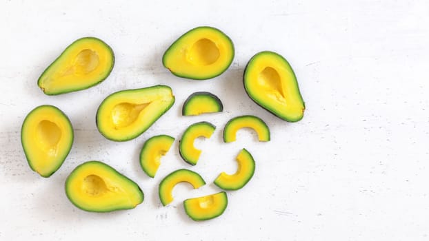 Top down view, avocado half and slices, on white working board, fruit pulp has vibrant green and yellow colour, space for text right.