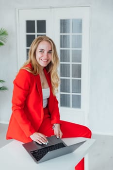 Woman in red suit with laptop in office