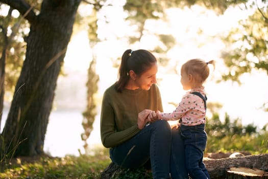 Smiling mom teaches a little girl to count on her fingers sitting on a stump in the forest. High quality photo