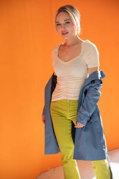 blonde woman in autumn raincoat on orange background