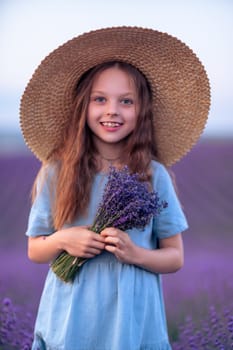 Lavender sunset girl. A laughing girl in a blue dress with flowing hair in a hat walks through a lilac field, holds a bouquet of lavender in her hands