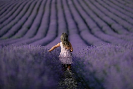 Lavender field girl. Back view happy girl in pink dress with flowing hair runs through a lilac field of lavender. Aromatherapy travel.