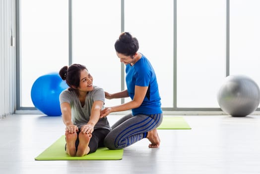 Asian young woman teacher teach adult student doing yoga stretching position in studio. Two woman teaching yoga and fun together, female sport fit workout concept