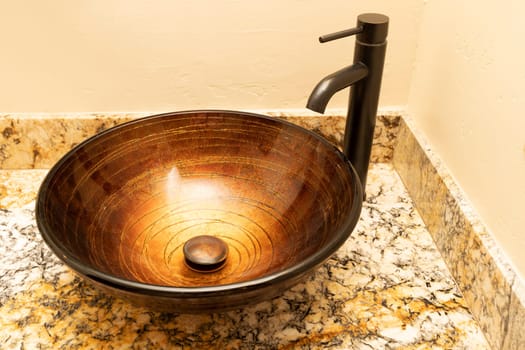 Golden Greek Glass Bowl Vessel Bathroom Sink And Faucet Set In Antique Rubbed Bronze Finish On Granite Countertop, Beige Walls. Close Up Bath Fixture. Horizontal. High quality photo