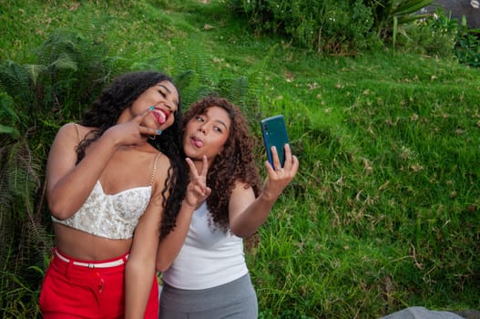 copy space of two teenagers taking a selfie with a funny expression with their tongues out and victory gestures with their fingers. High quality photo